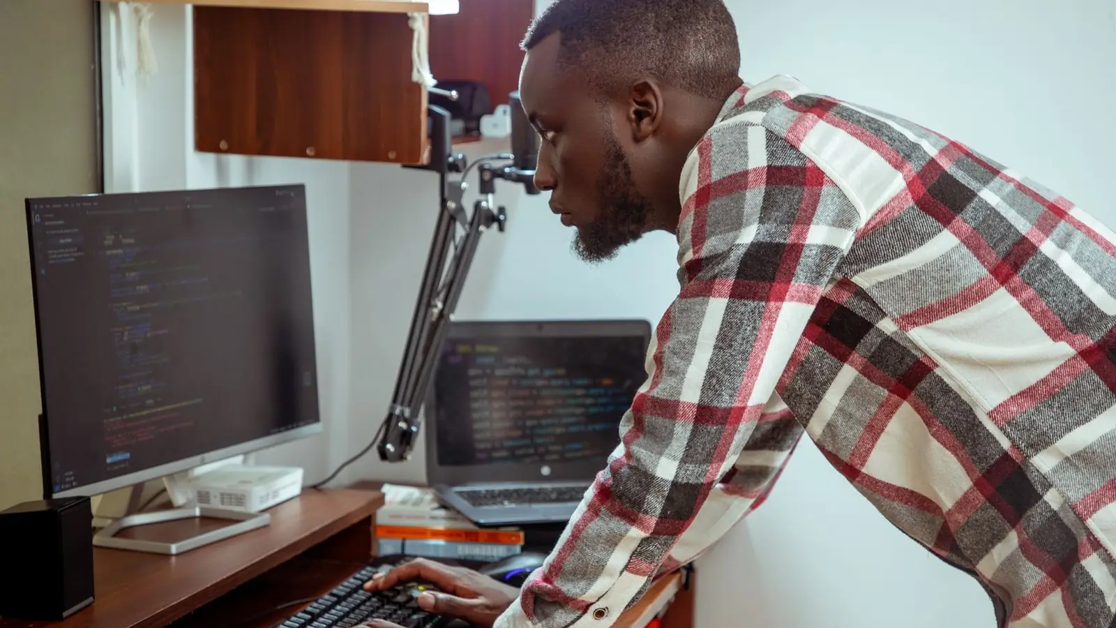 A software developer in Nairobi working across a laptop and a desktop monitor full of code